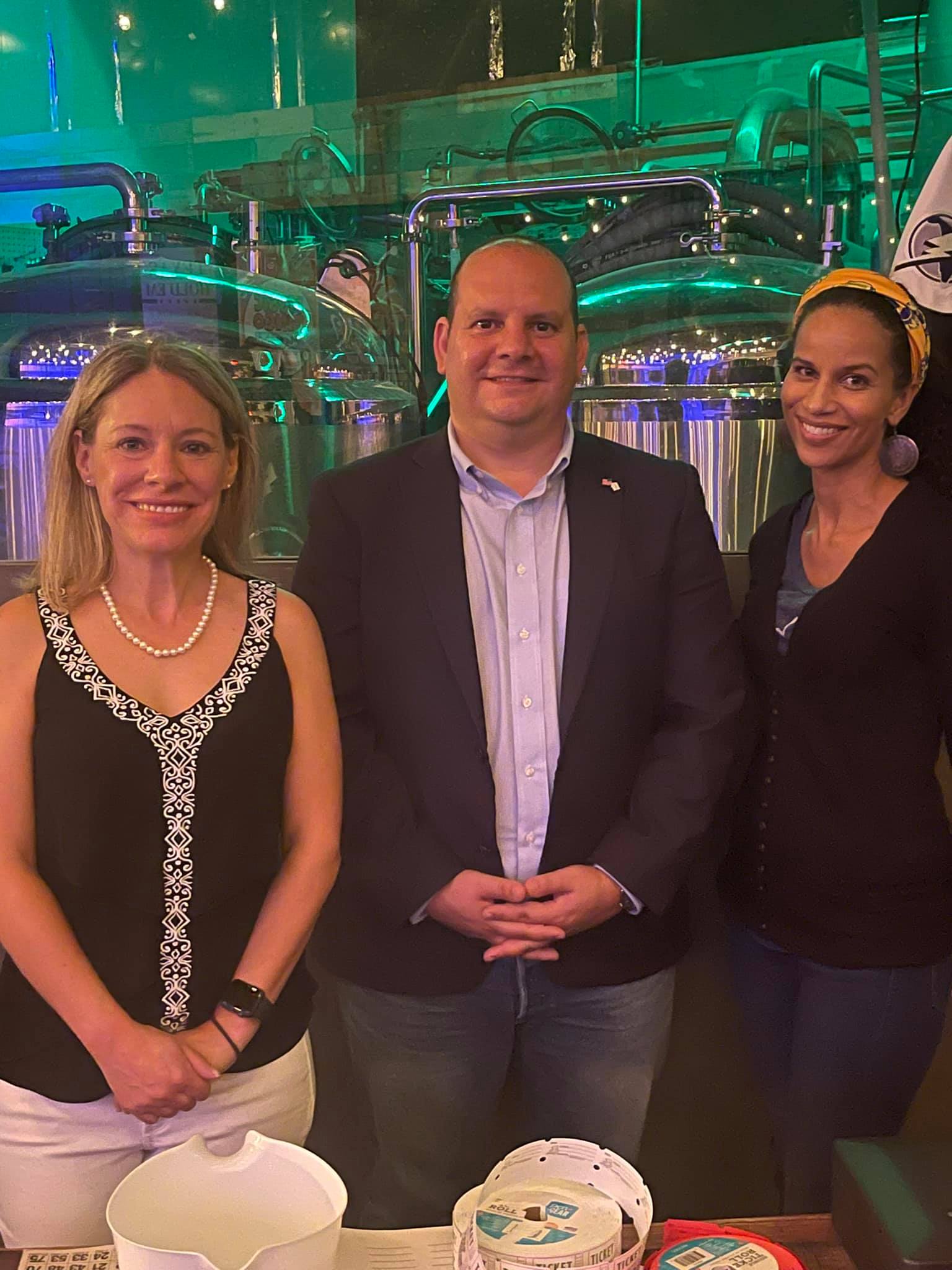 Three people posing for a photo in front of a green-lit, industrial-looking background.