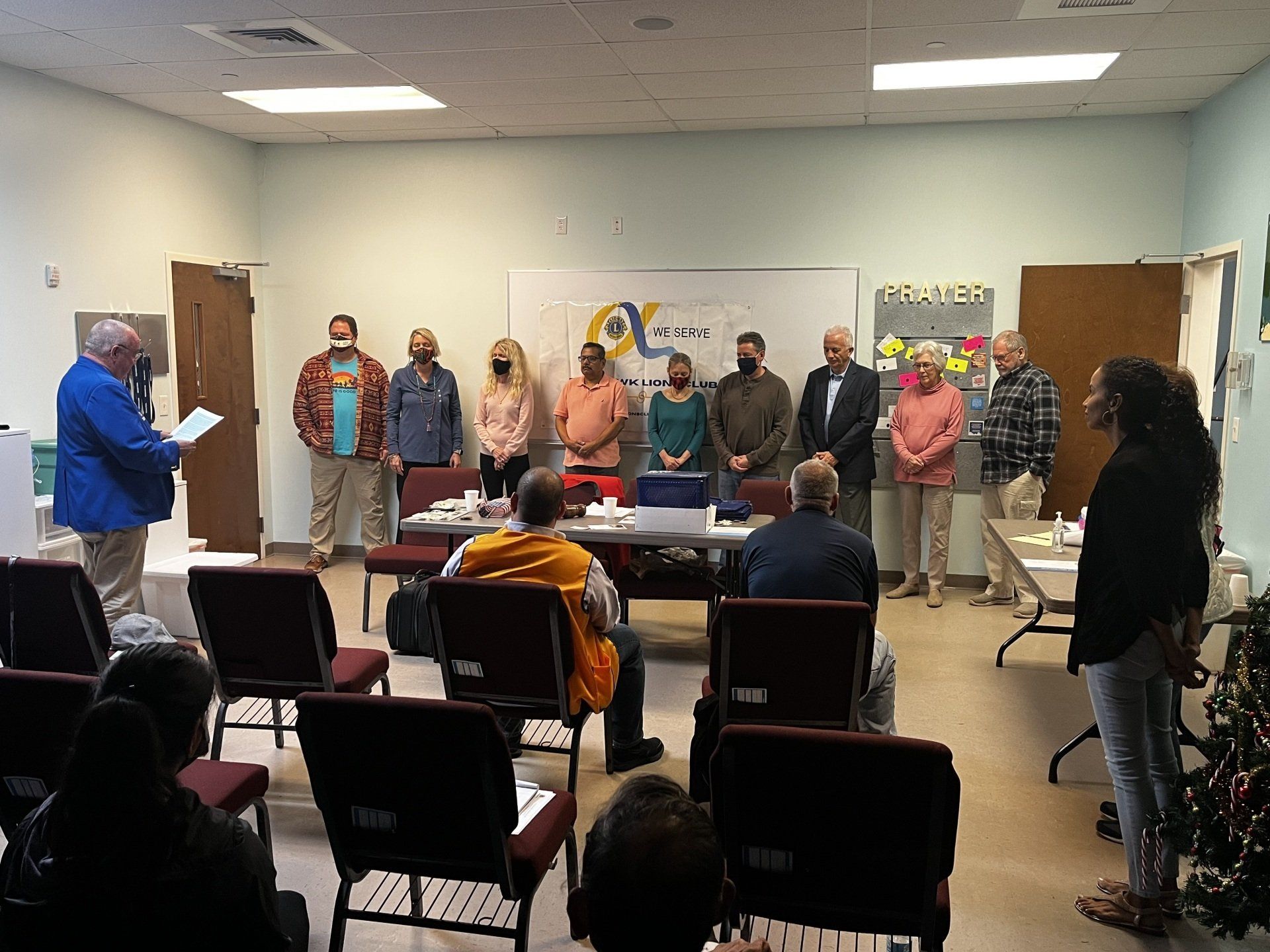 People standing in a room for a ceremony, some reading, others listening.