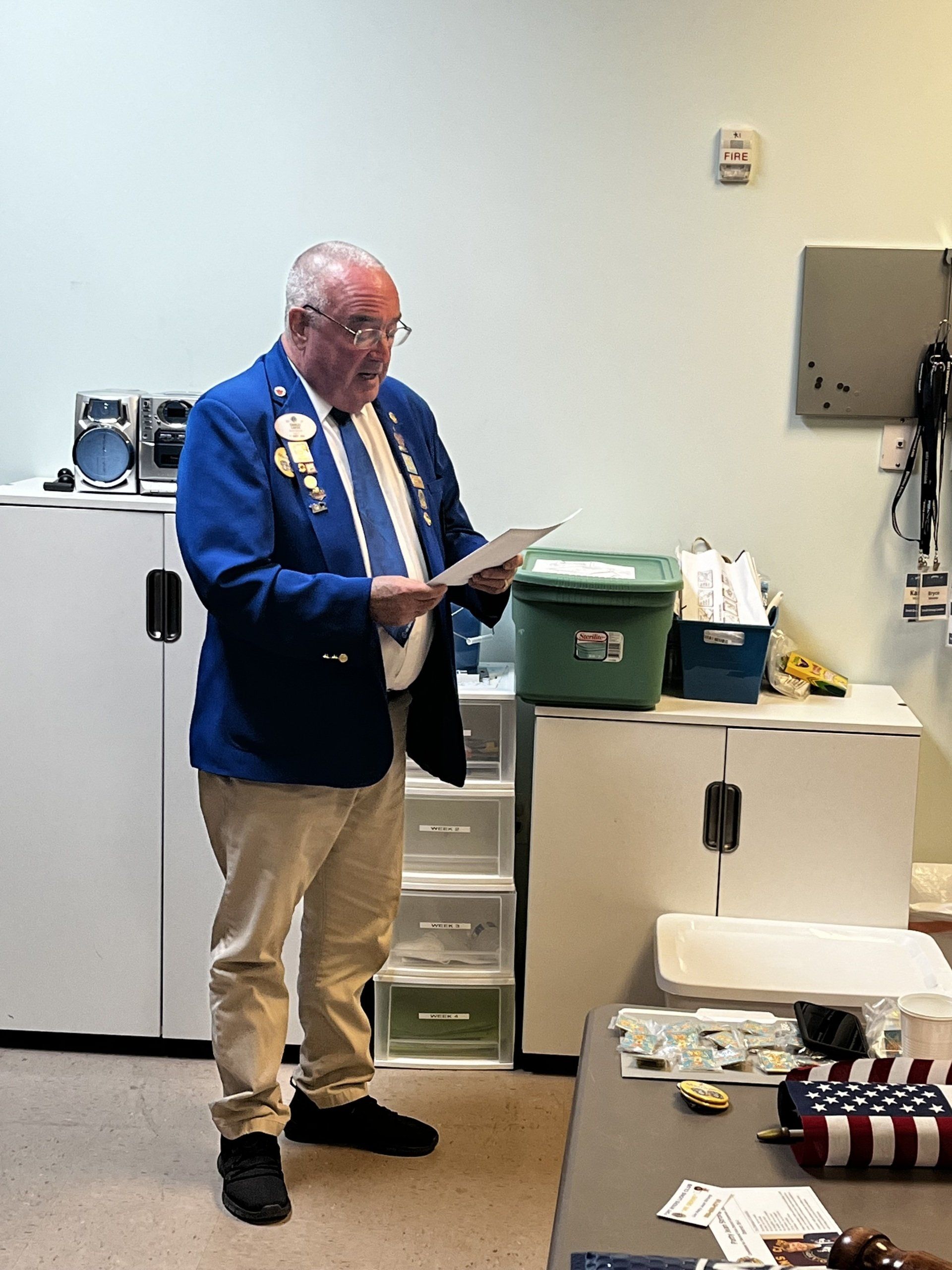 Man in blue jacket, reading papers in a room with cabinets.