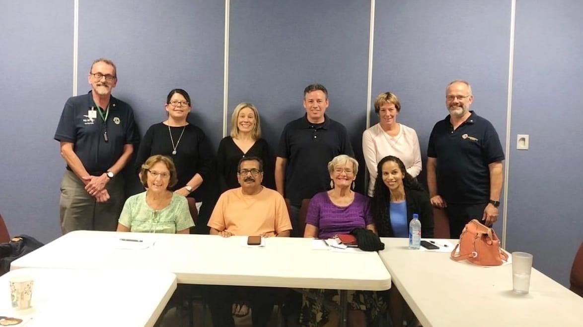 Group of diverse people in a meeting room, smiling and posing at a table in front of a blue wall.