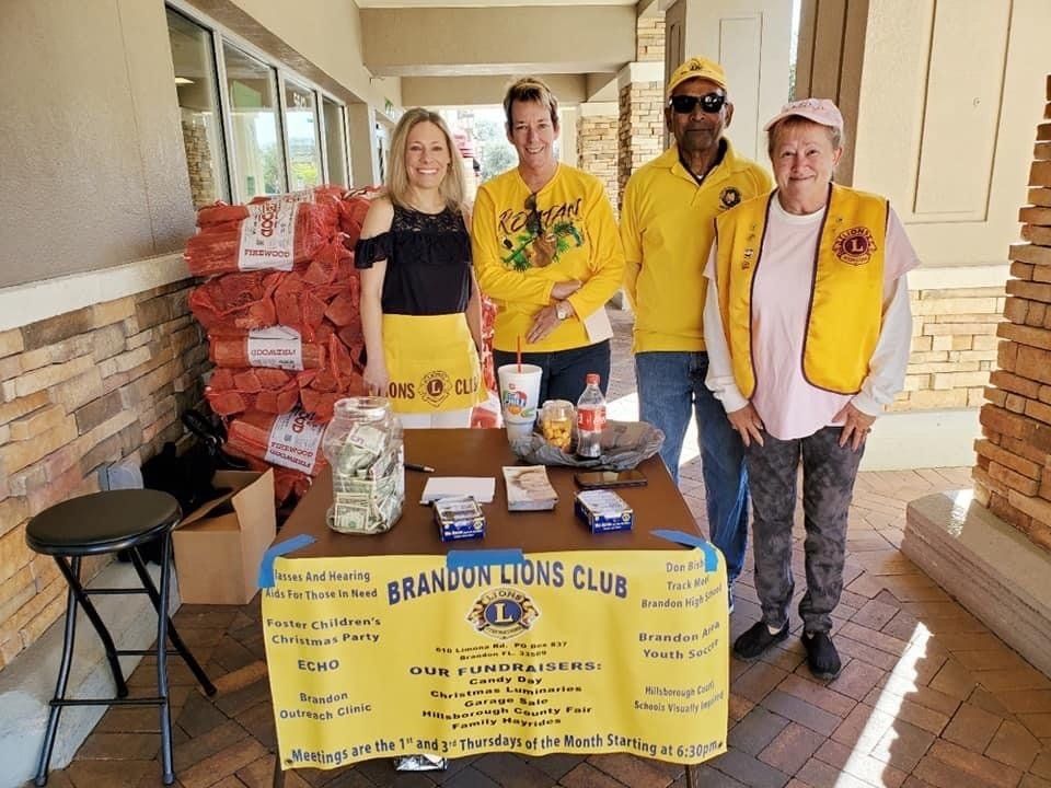 Four people at a Brandon Lions Club fundraising table. They are wearing yellow. Bags of onions are for sale.