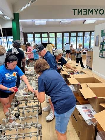 Volunteers sorting items from boxes in a brightly lit room, possibly a community center.