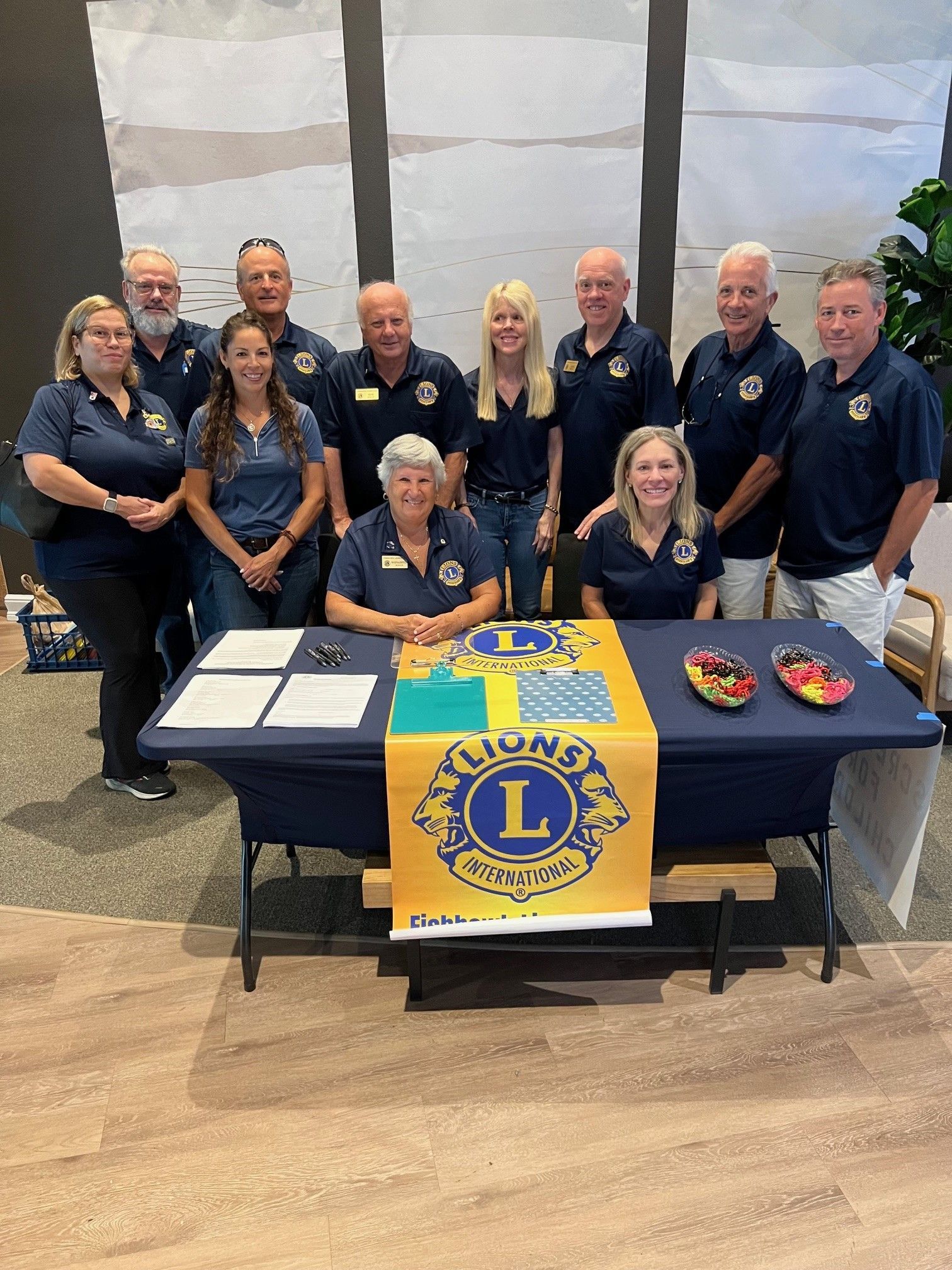 Group of Lions Club members at a table, blue shirts, yellow banner, signing papers.