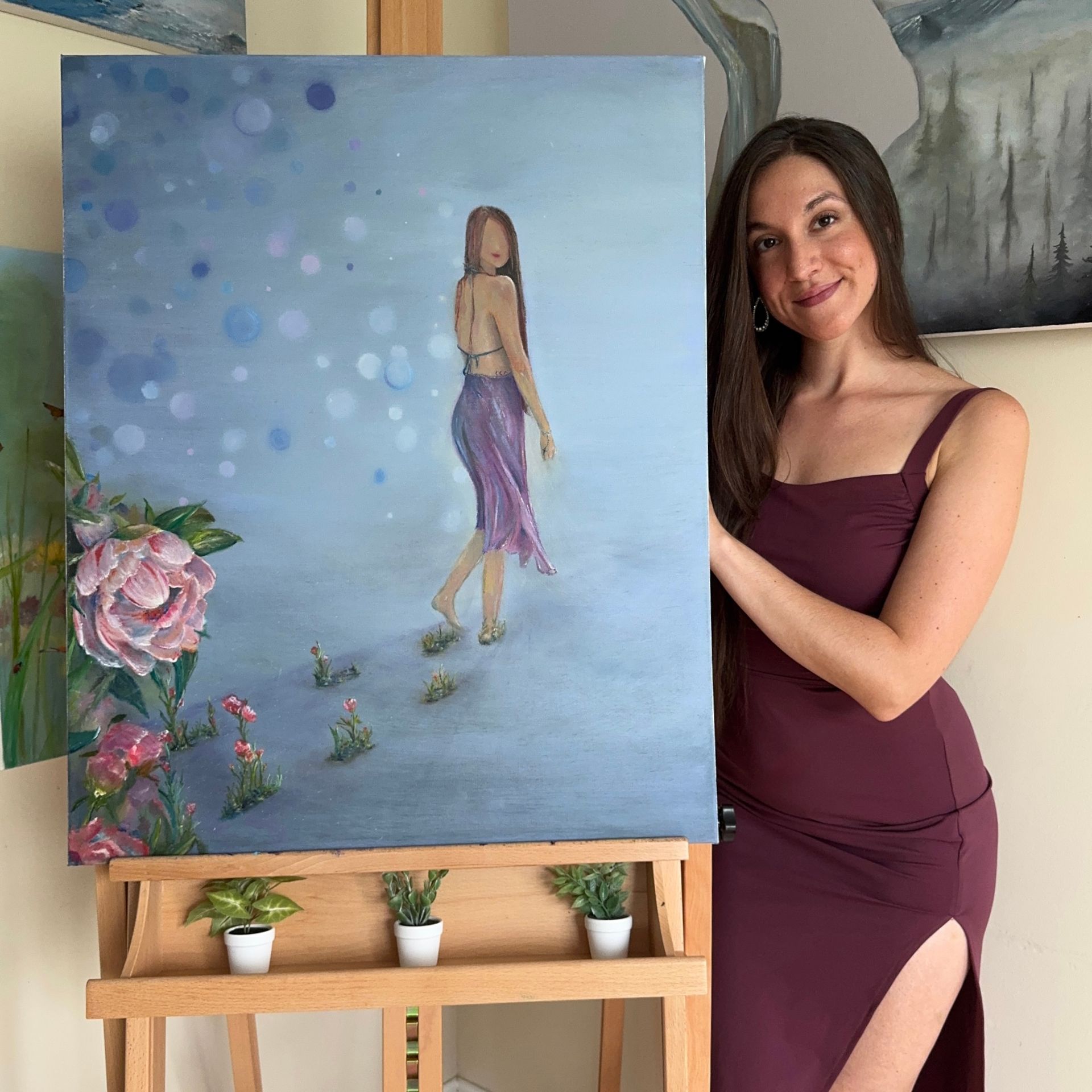 A woman is holding a painting on an easel.