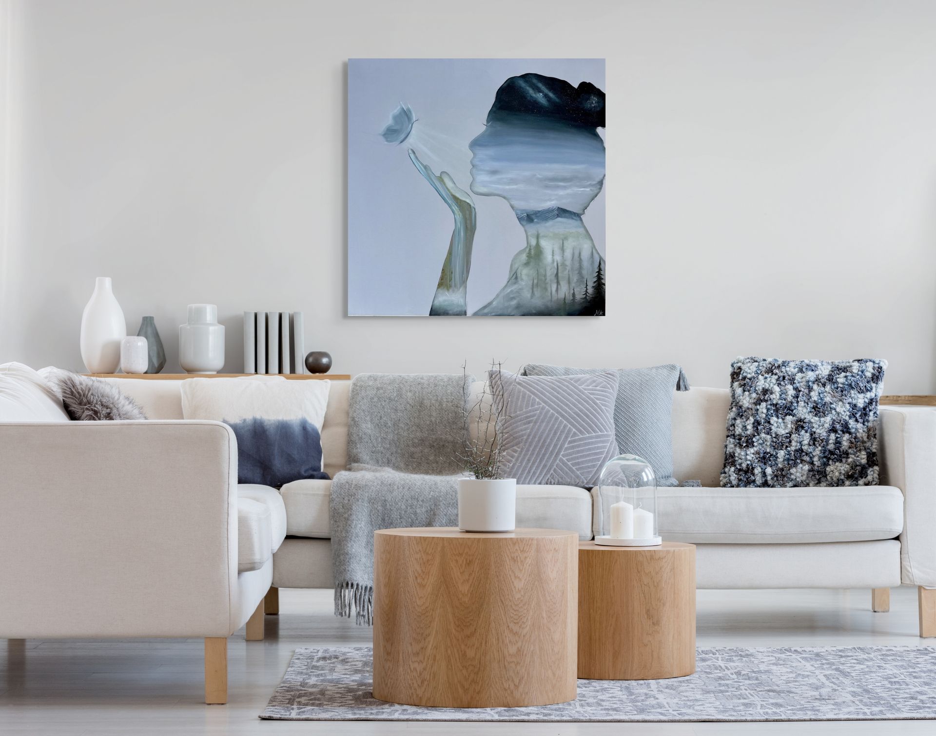 original painting by Nicole Ann of a woman's silhouette being lit by a butterfly hovering above her hand revealing a landscape scene inside her that consist of a galaxy, clouds, a mountain range, foggy pine trees, and a waterfall on a stretched canvas displayed in a living room