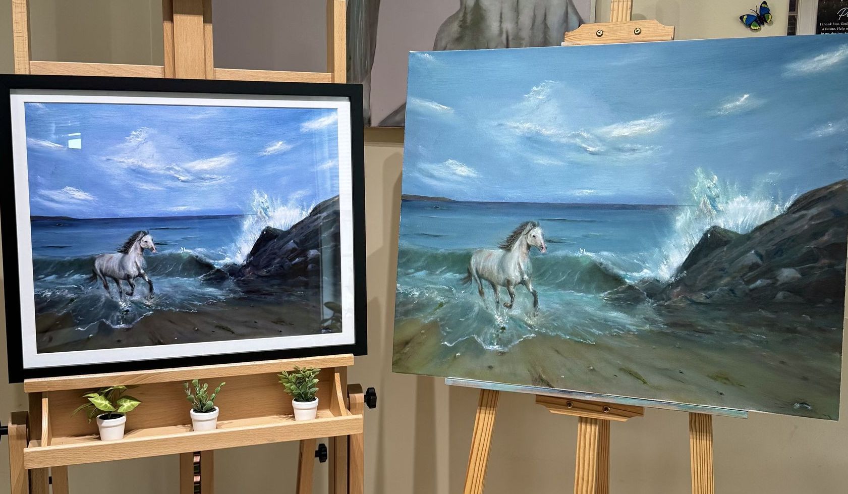 Two paintings of a horse on a beach are on an easel.