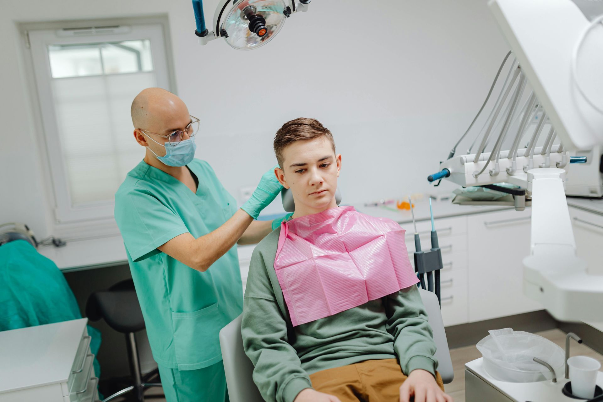 A young man is sitting in a dental chair while a dentist examines his teeth.