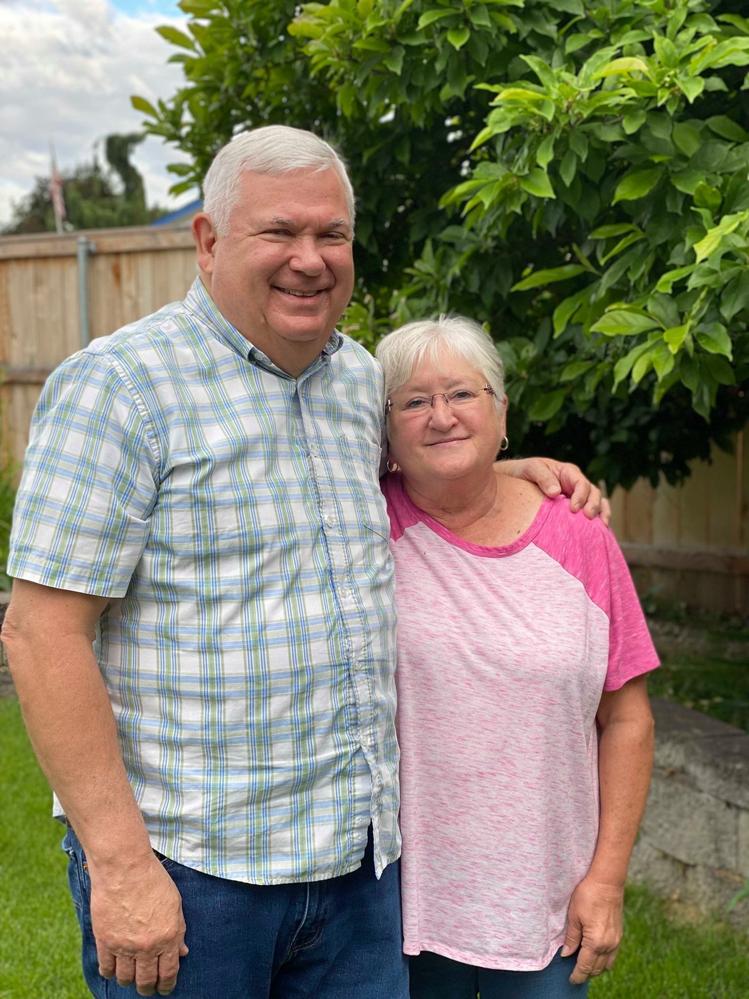 Man and woman standing together in a backyard. The man has his arm around the woman. Both are smiling.