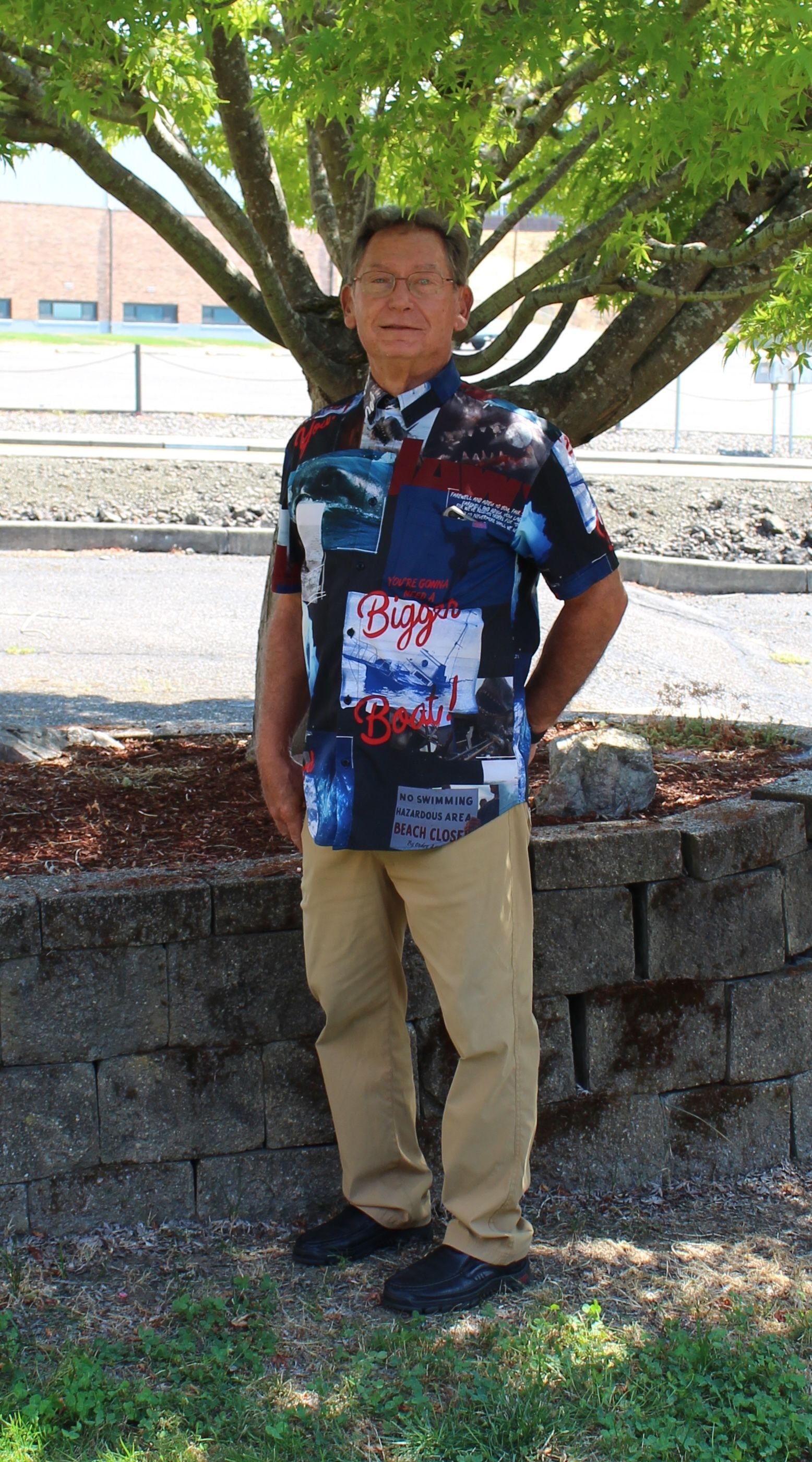 Man standing in front of a tree, wearing a patterned shirt and khaki pants.