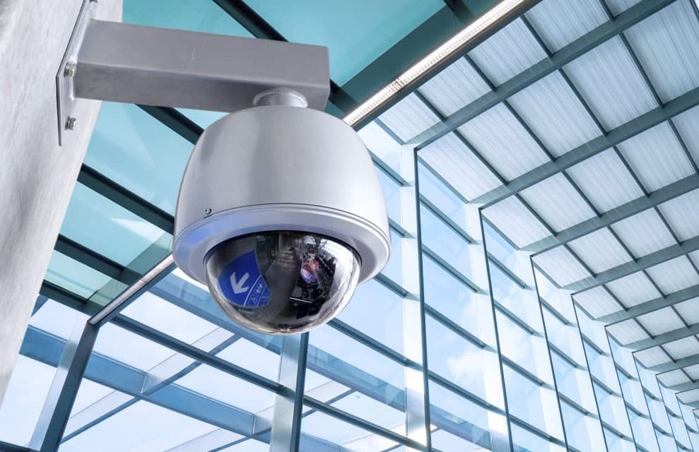 Security Camera Mounted on a Wall, Overlooking a Modern Building With Glass Ceiling — IRIS CCTV in Coffs Harbour, NSW