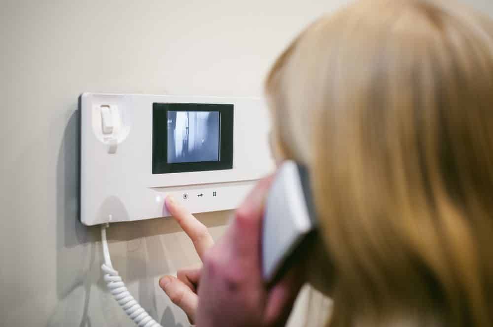 Woman Using a White Intercom With a Screen While Pressing a Button and Holding the Phone to Her Ear — IRIS CCTV in Coffs Harbour, NSW