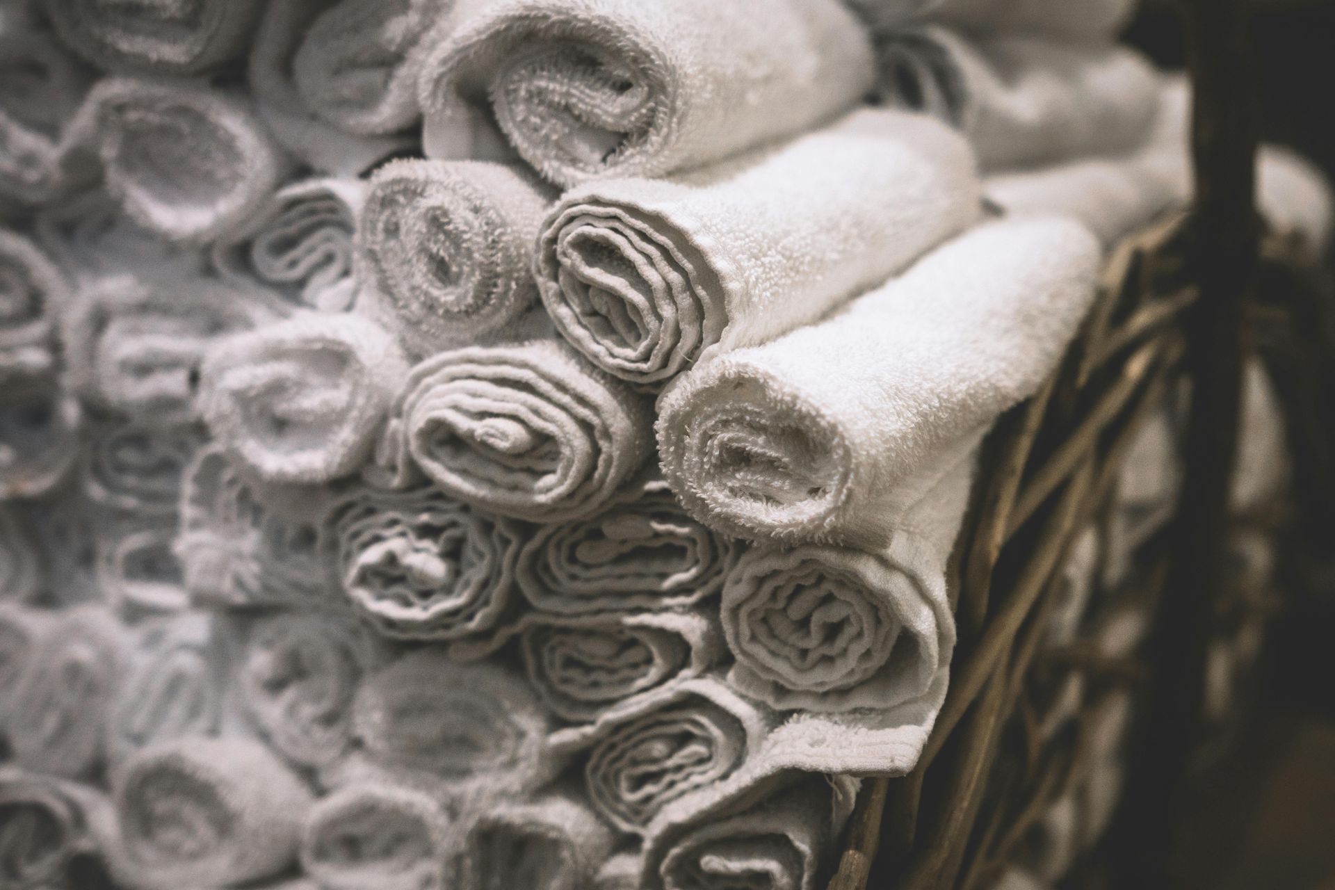 A clean pile of white towels rolled up in a basket by Mountain Tops Cleaning Service.