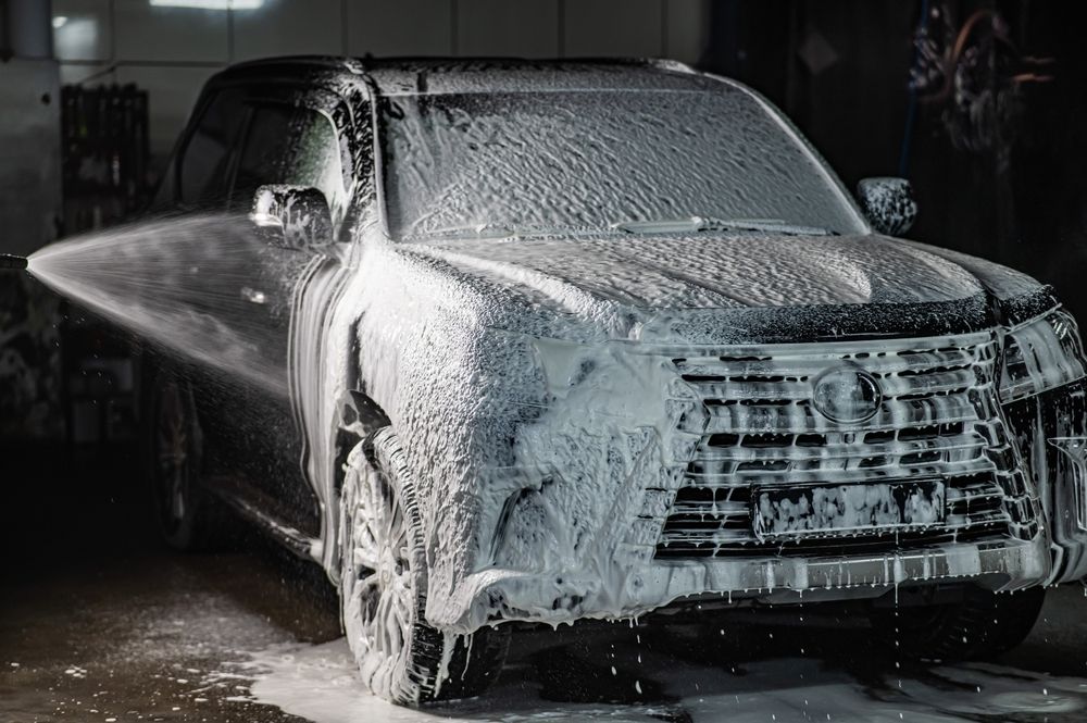 Black pickup truck covered in white foam being washed at a car wash.