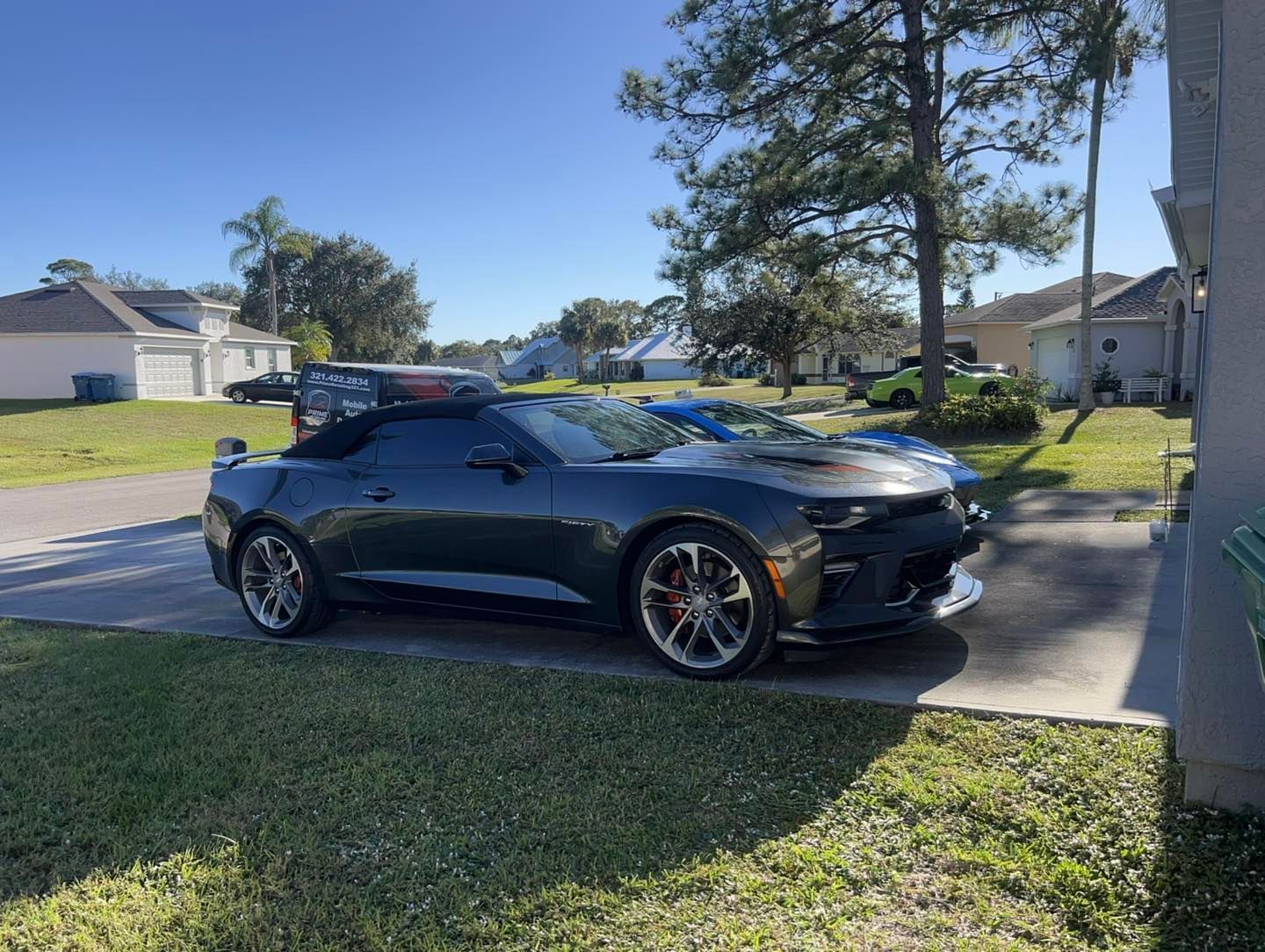 Dark gray convertible car parked on a residential street on a sunny day.
