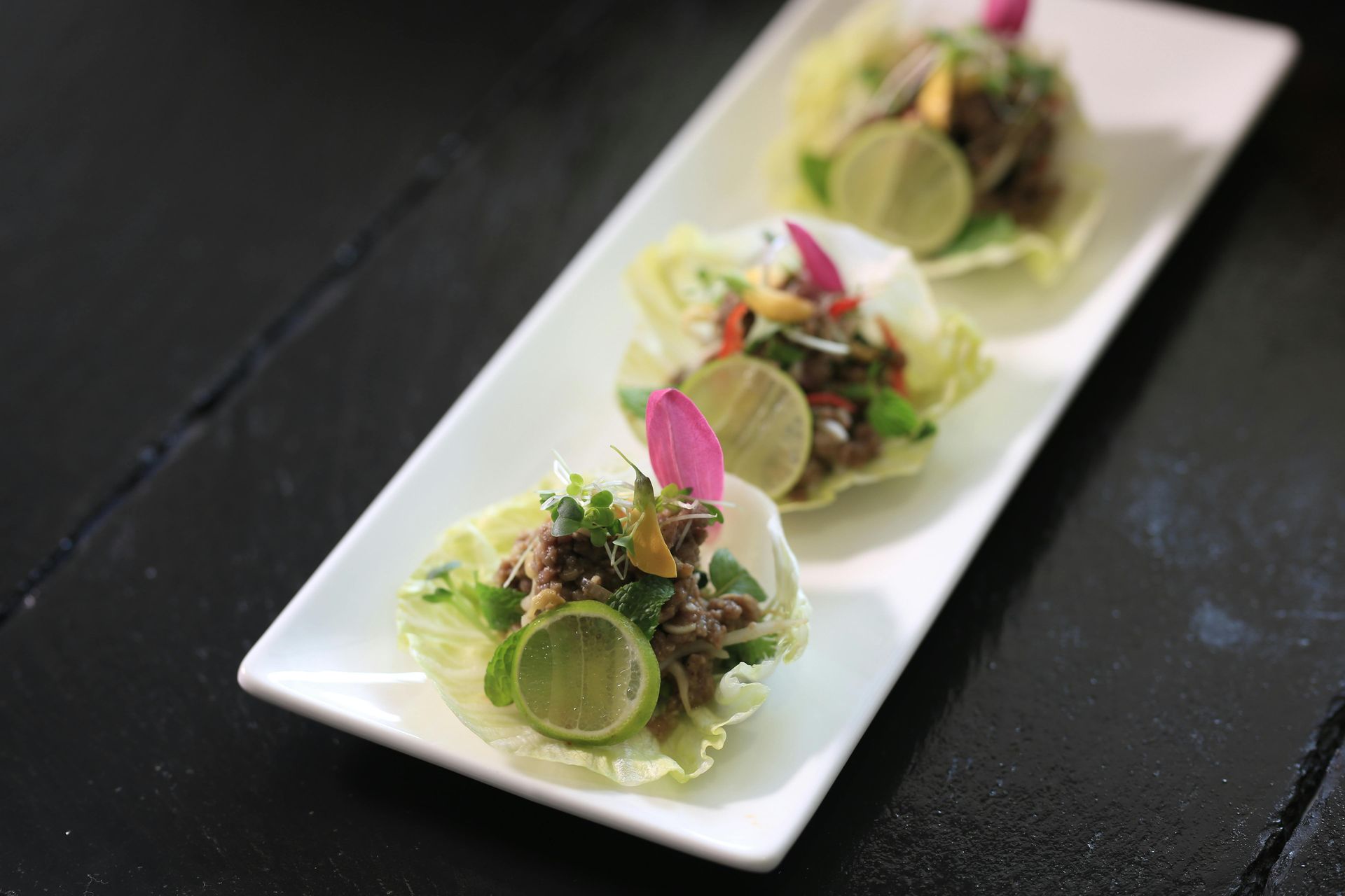 Three appetizers, each in lettuce cups, garnished with lime and flowers.