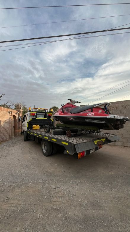 Una moto acuática roja descansa sobre una grúa de plataforma en un camino de tierra bajo un cielo nublado.