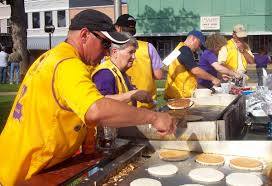 People in yellow vests cooking pancakes outdoors at a community event.