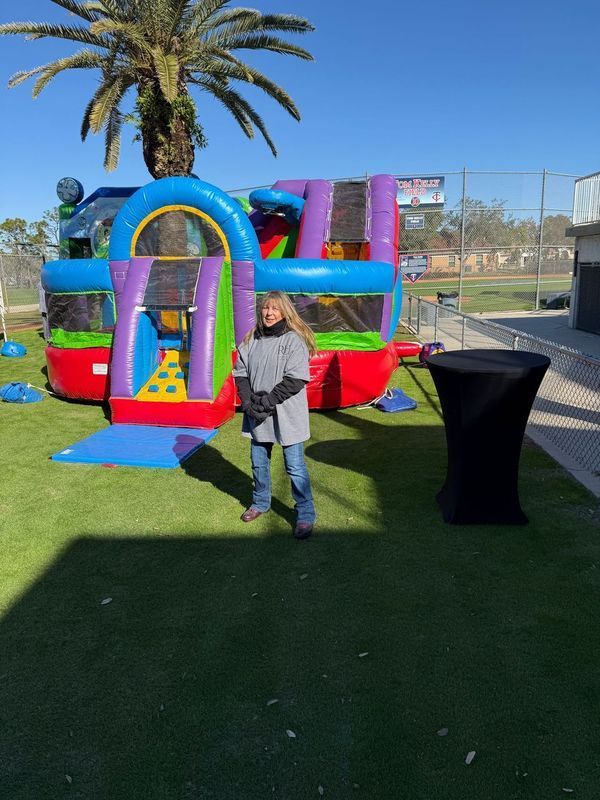 Person standing in front of a colorful inflatable bounce house on green turf under a sunny sky.