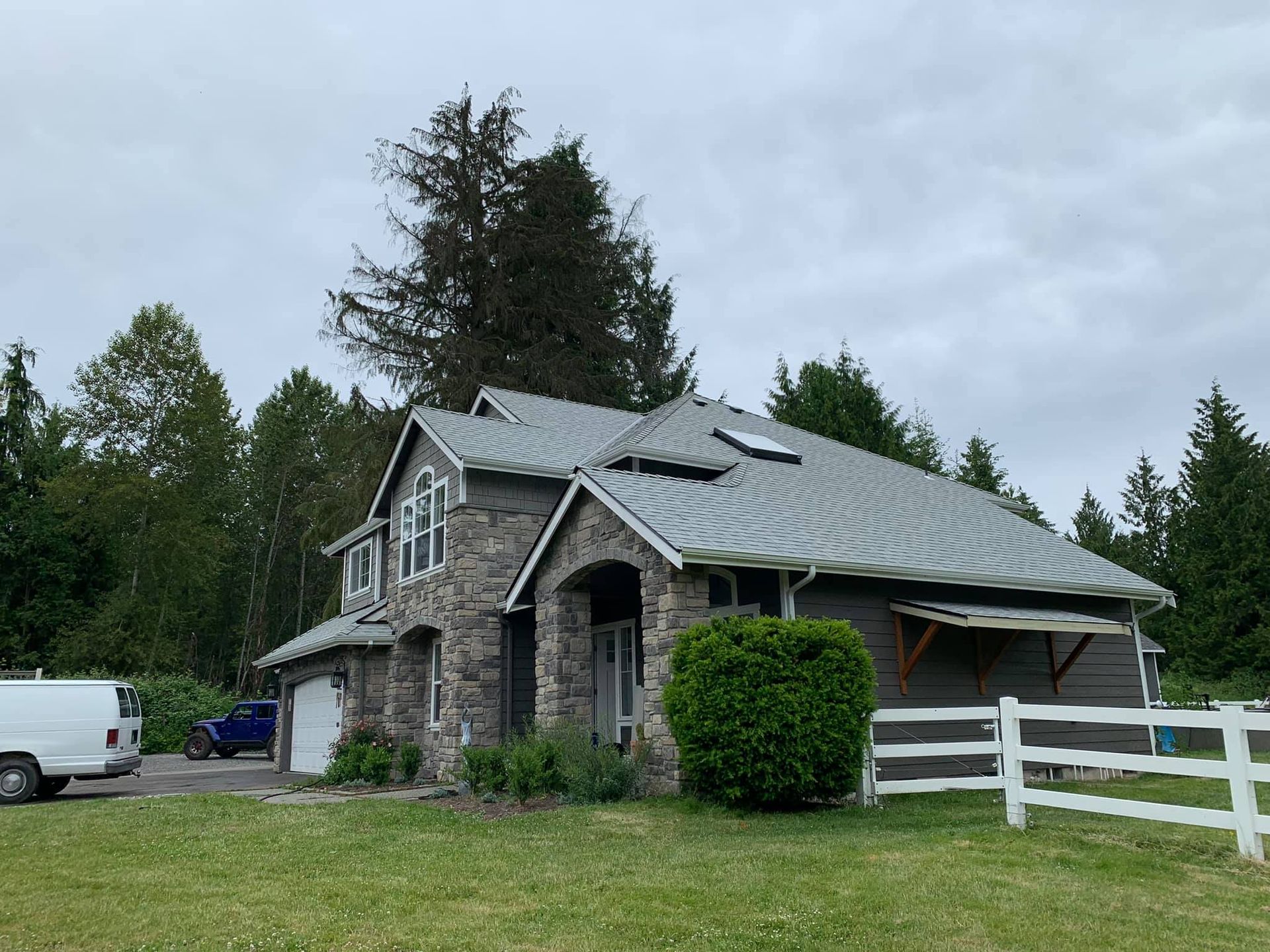 A large house with a metal roof is surrounded by trees and a white fence.