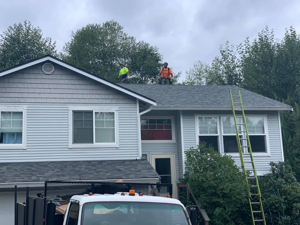 A white truck is parked in front of a house with two men on the roof.