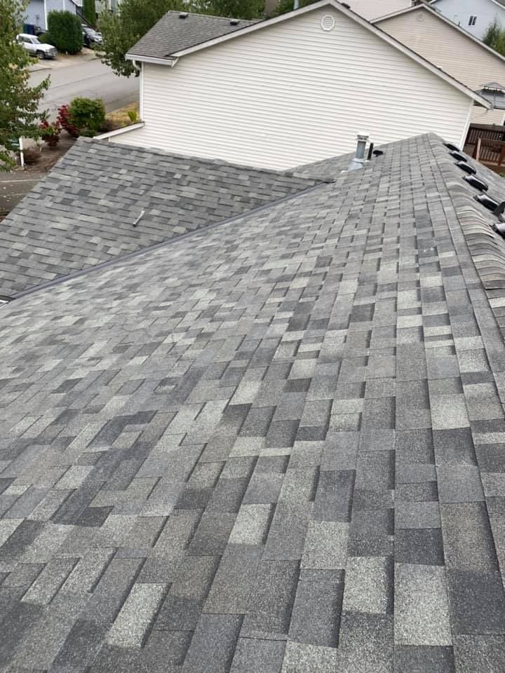 A roof with a lot of shingles on it and a white house in the background.