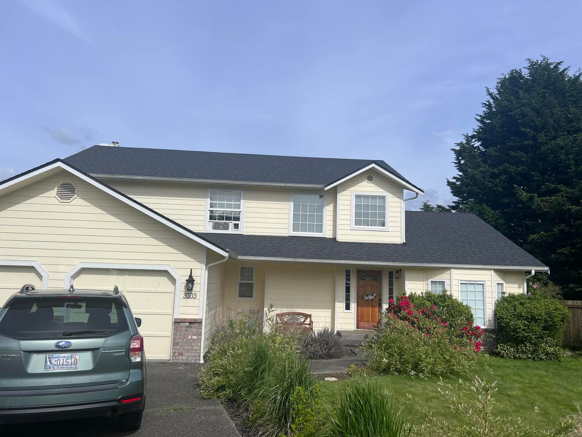 A car is parked in front of a white house with a black roof.