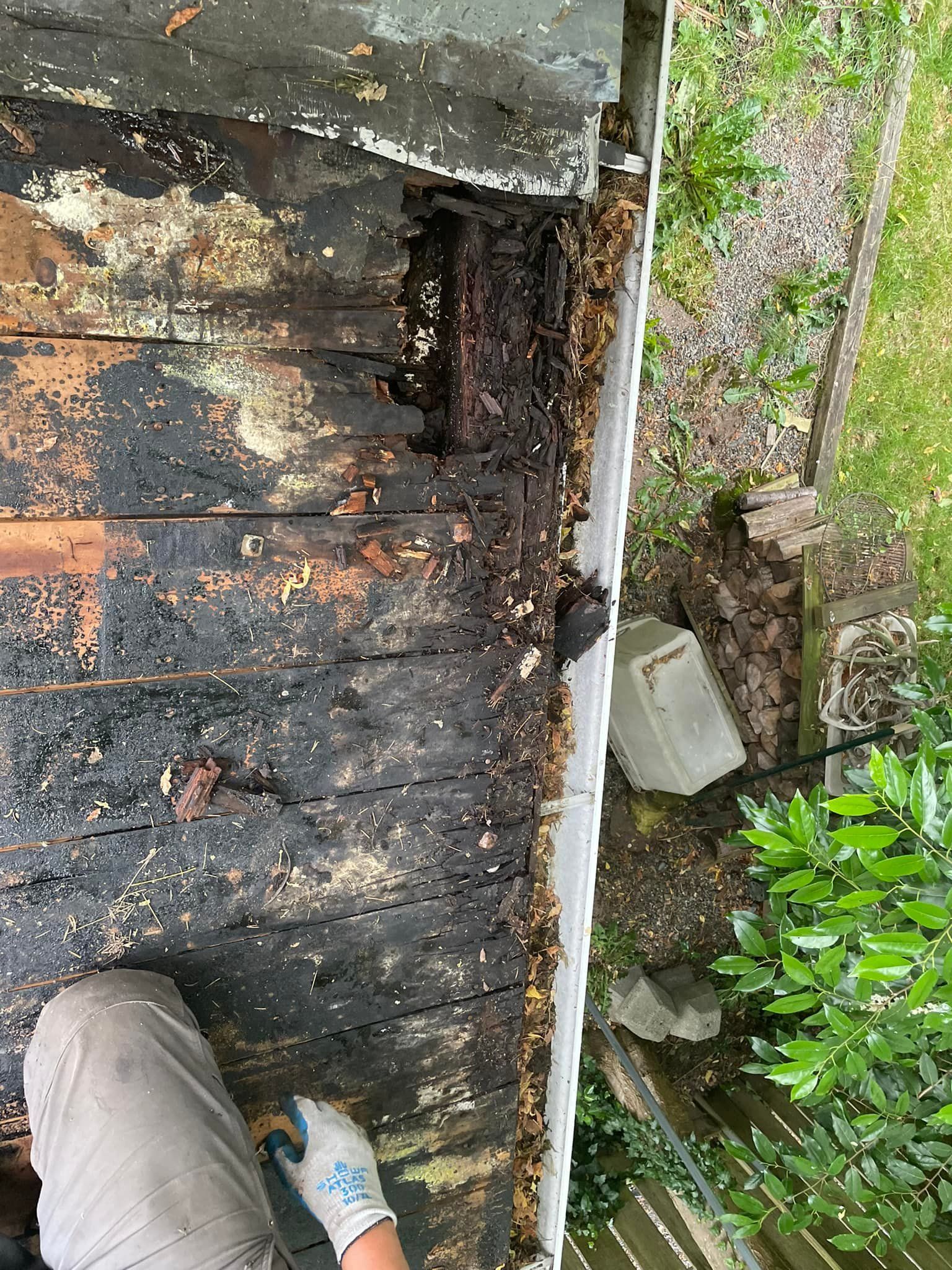 A person is working on a wooden roof next to a gutter.