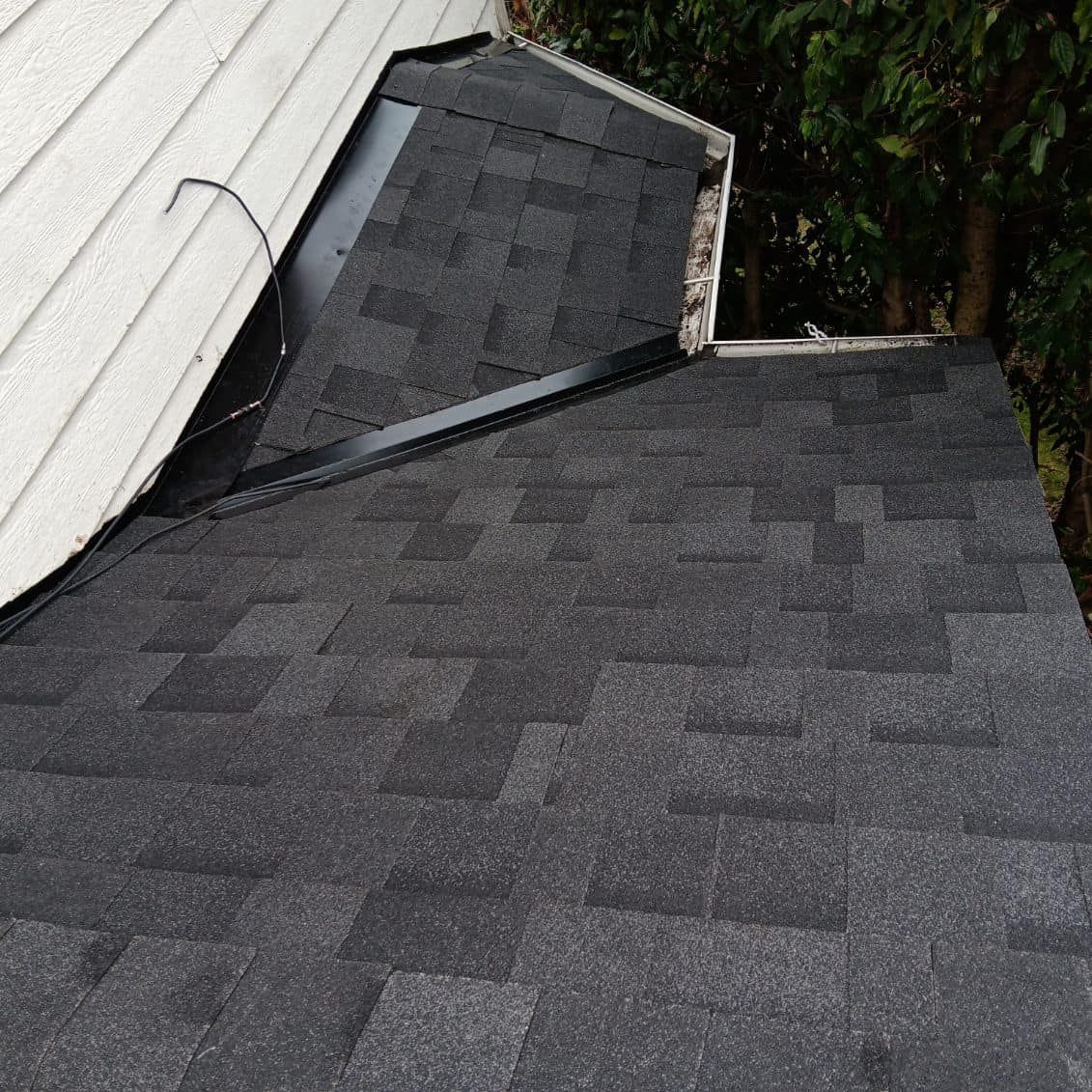 A close up of a black roof with a white house in the background.