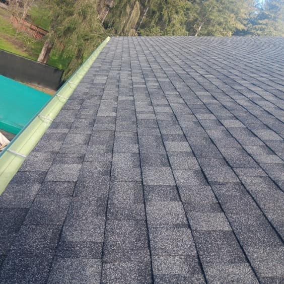 A close up of a roof with shingles and a green gutter.
