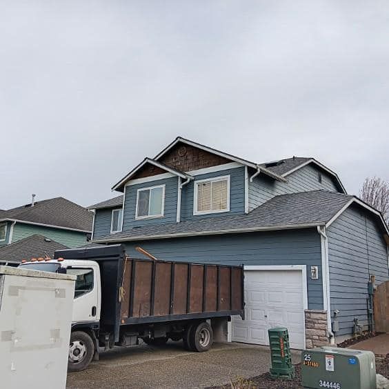 A dump truck is parked in front of a blue house.