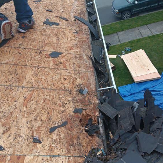 A person is standing on top of a roof with a lot of shingles on it.