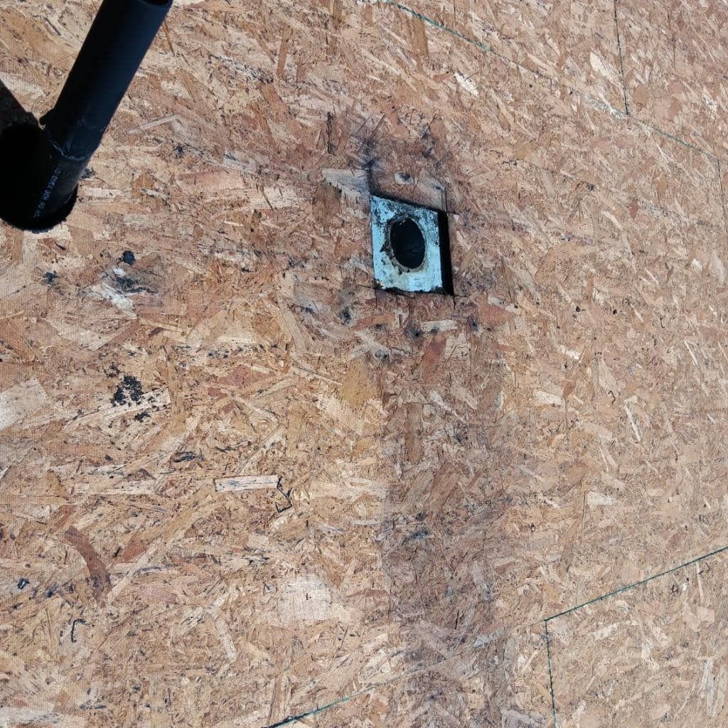 A hole in a piece of plywood with a pipe coming out of it.