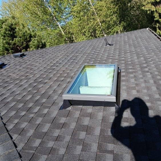 A man is taking a picture of a skylight on a roof.