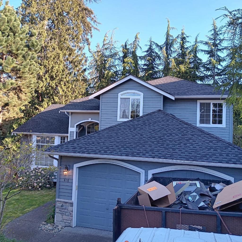 A large gray house with a black roof is surrounded by trees.