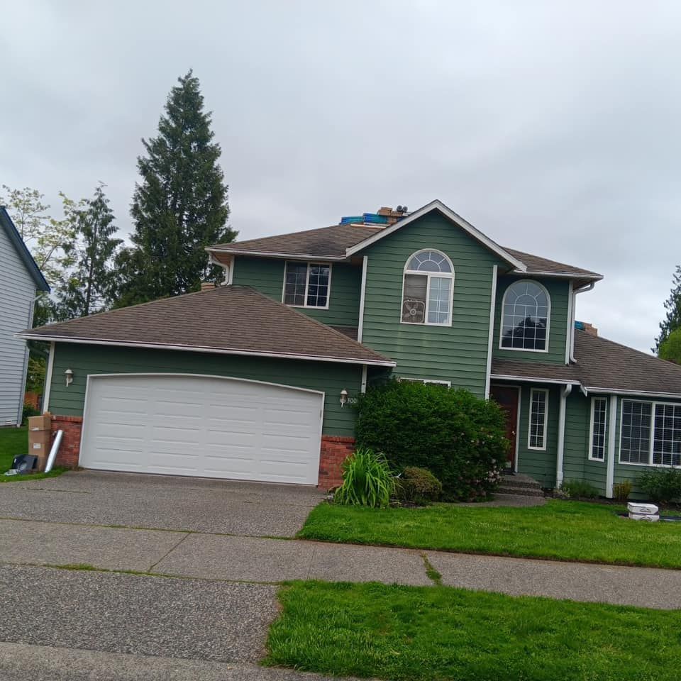 A green house with a brown roof and a white garage door