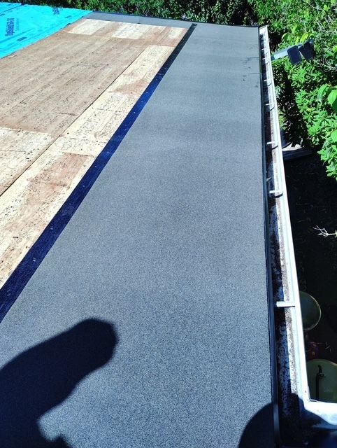 The roof of a house with a balcony and trees in the background.