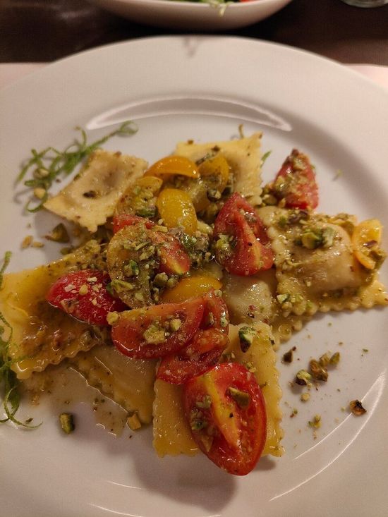 Interno di un ristorante moderno con tavoli, sedie e piante su pareti grigie e gialle.