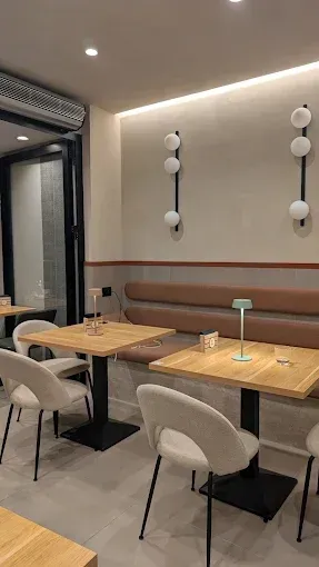 Interno di un bar con tavoli, sedie, sedute integrate e luci decorative da parete.