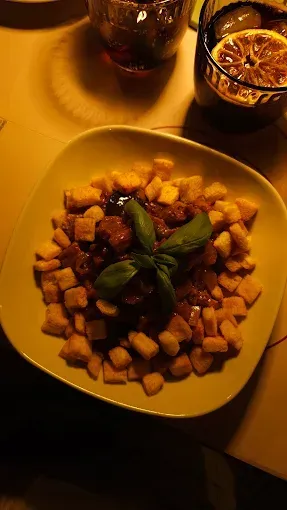 Piatto di gnocchi con ragù di carne e guarnizione di basilico, servito con bevande su un tavolo.