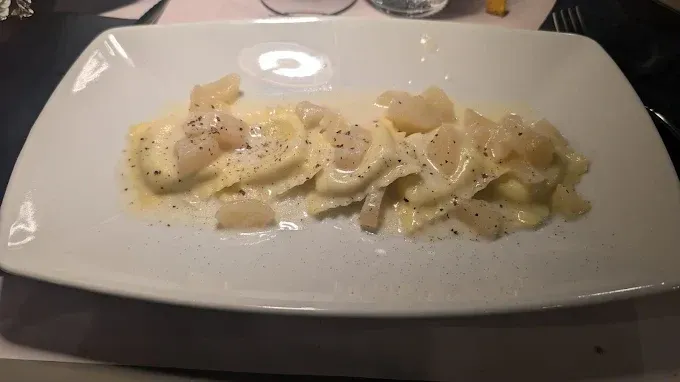 Piatto di pasta ravioli in salsa bianca cremosa, guarnito con pepe e pezzetti di formaggio su un piatto bianco.