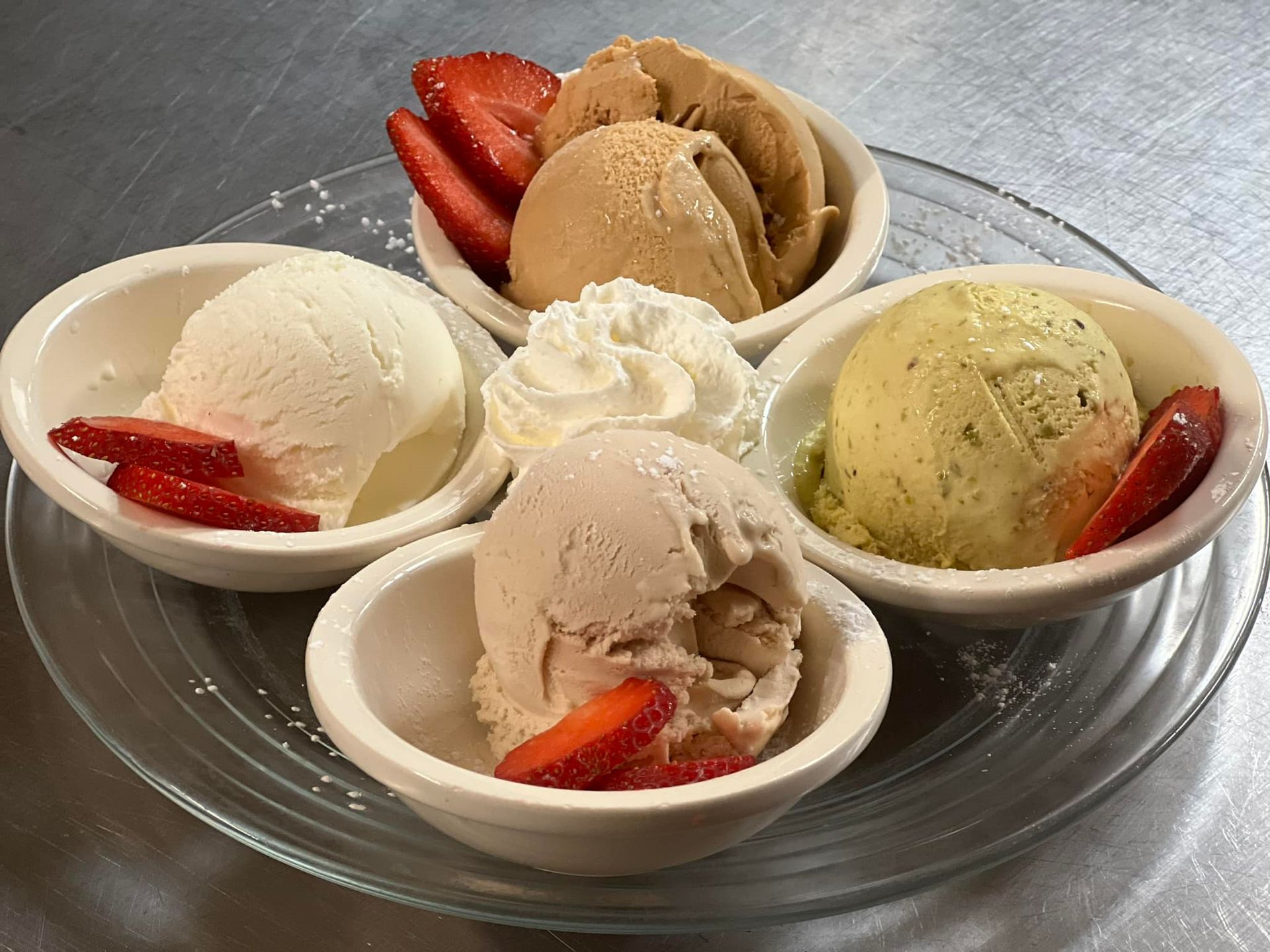 Four bowls of ice cream with strawberries and whipped cream on a plate.