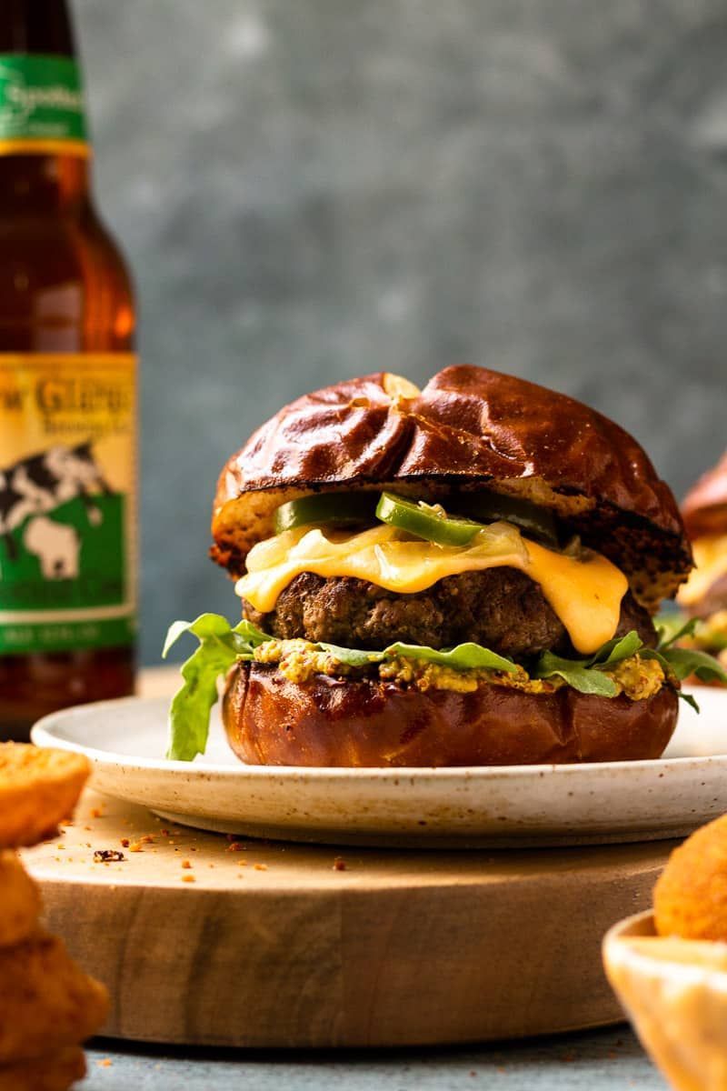 A close up of a hamburger on a plate with a bottle of beer in the background.