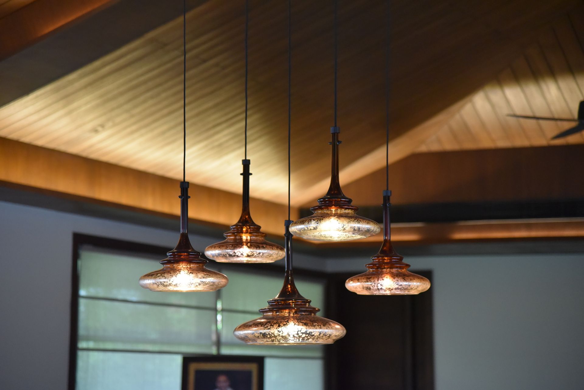 Five copper-colored pendant lights hang from a wood-paneled ceiling, illuminating the space below.