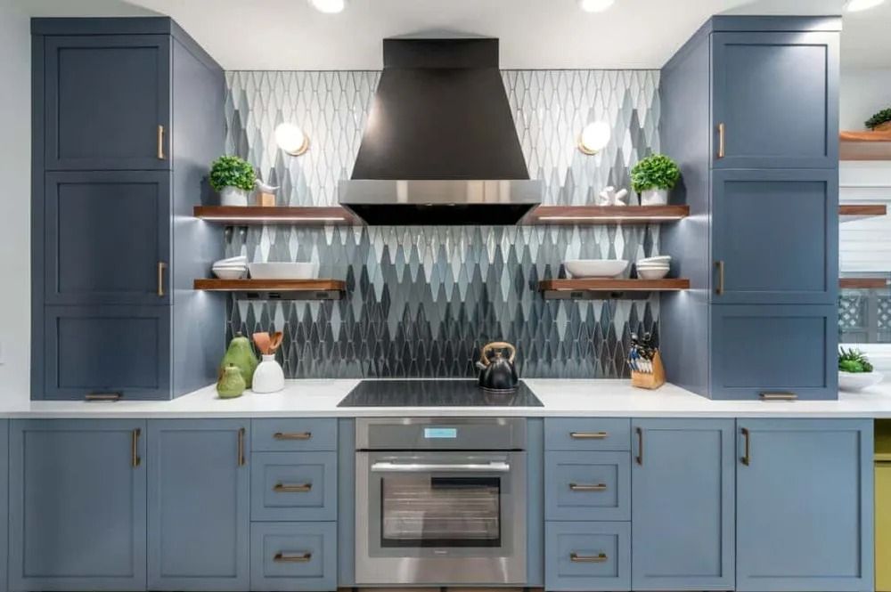 Blue kitchen with white countertops, stainless range hood, patterned backsplash, and open shelves with plants.