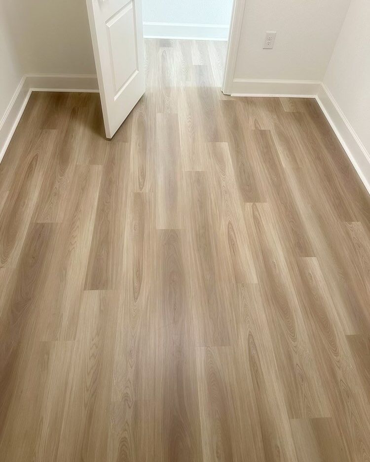 Empty room with light wood flooring and an open white door leading to a brighter hall.