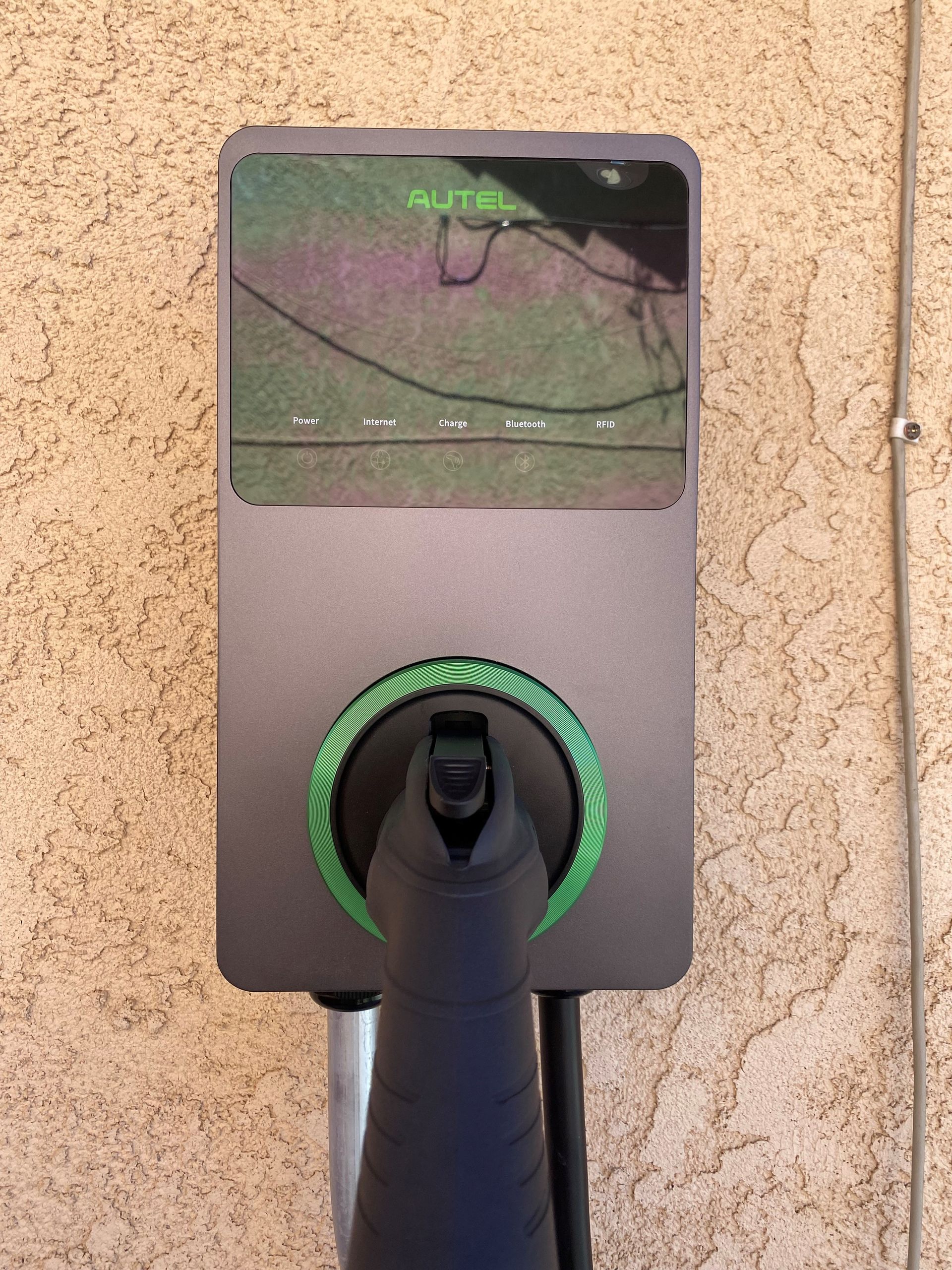 A black device with a green circle on it is attached to a wall.