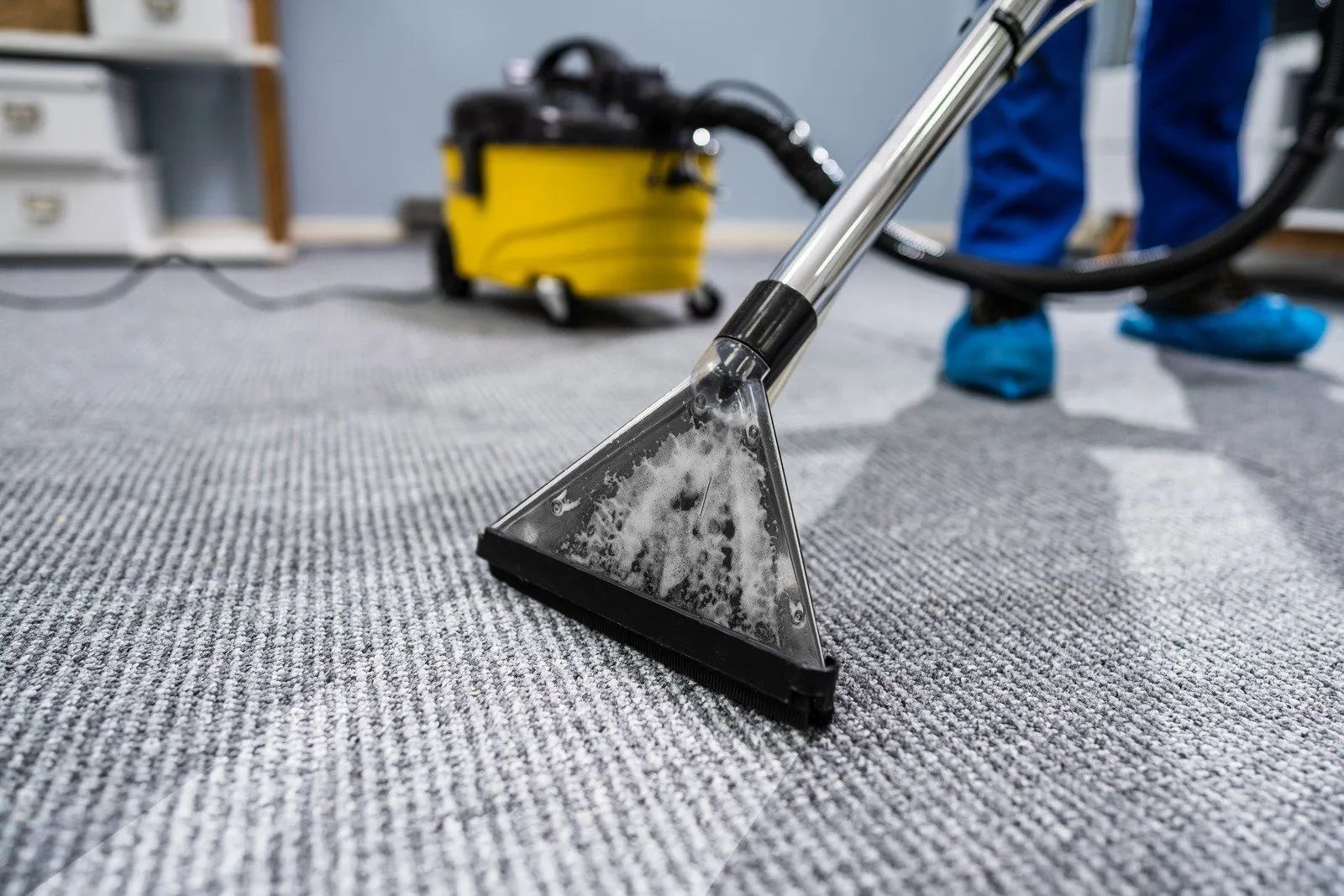 Carpet cleaner vacuuming a gray rug in a commercial cleaning setting
