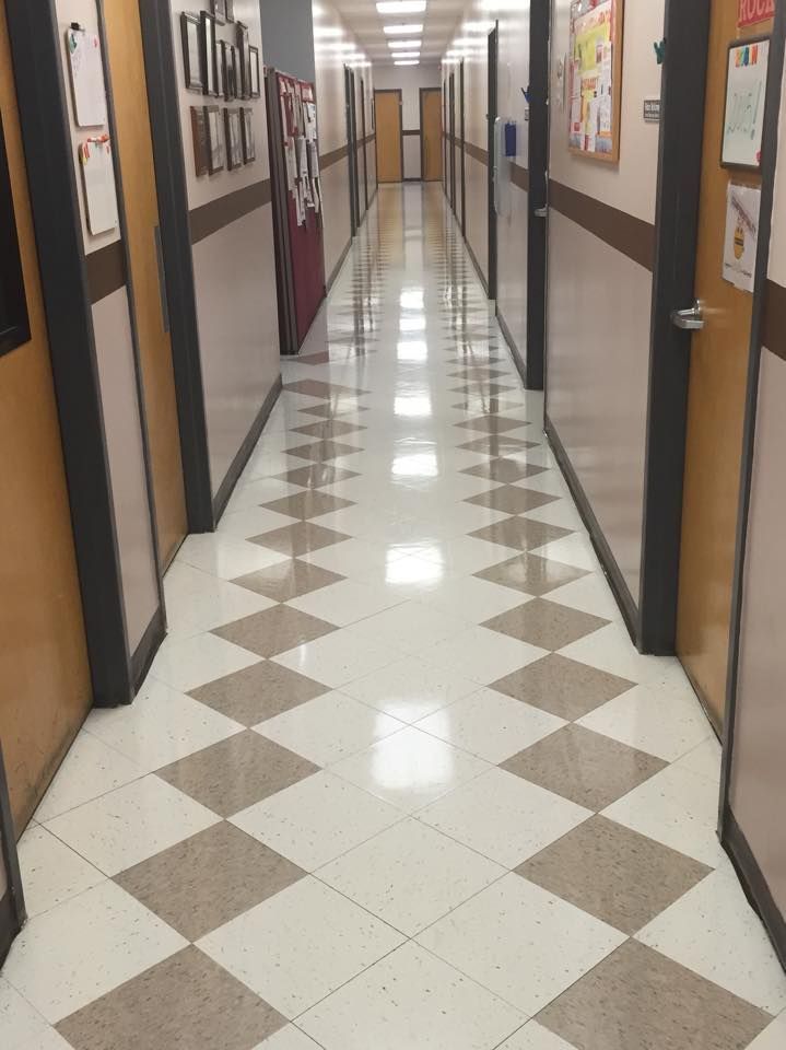Long hallway with diamond-patterned floor, doors, and bulletin boards on walls.