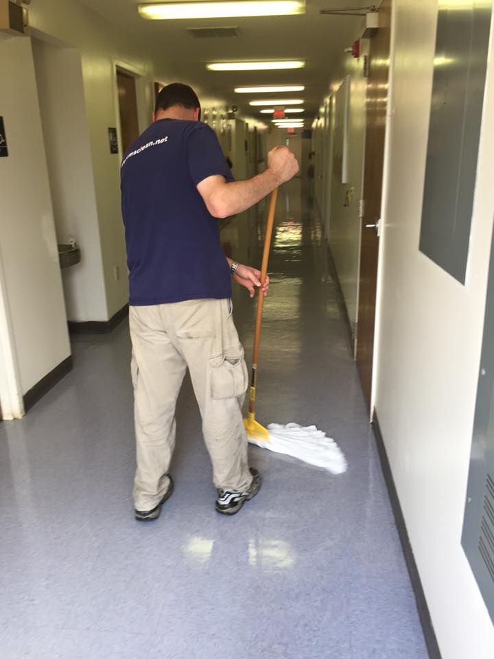 Person mopping a hallway floor; the floor is light blue and walls are white.