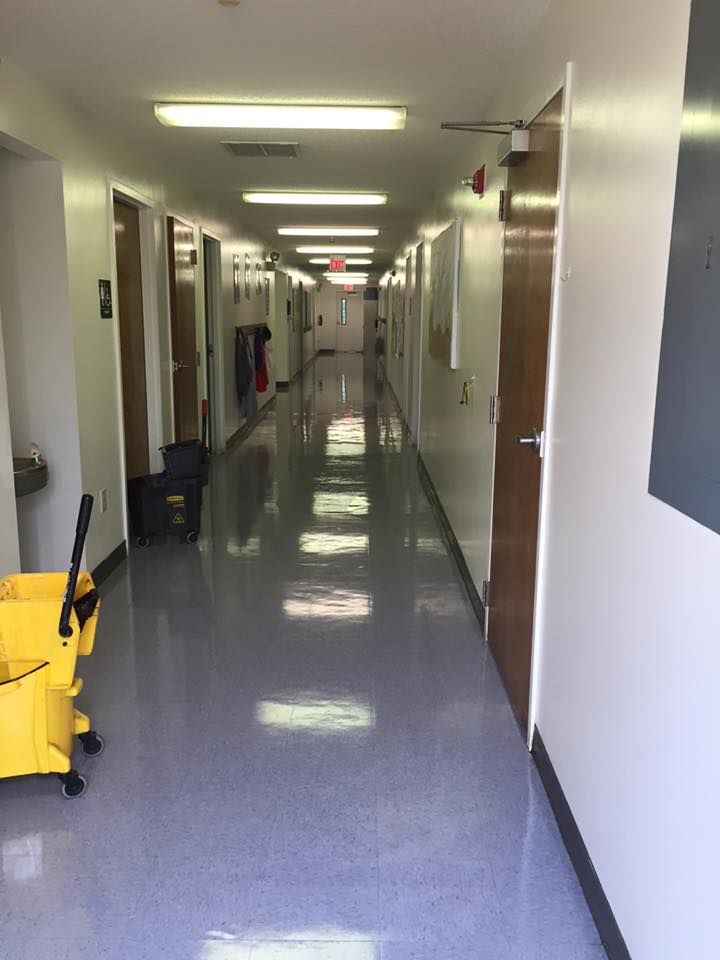 Long, empty hallway with doors, overhead lights, and a yellow cleaning cart.